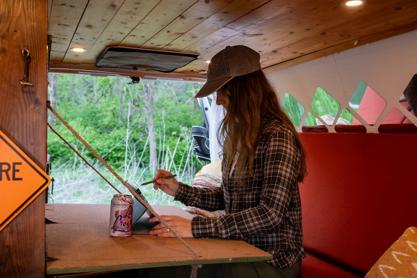Working remotely in an RV rental: A woman uses a tablet in a cozy van, enjoying forest views outside.