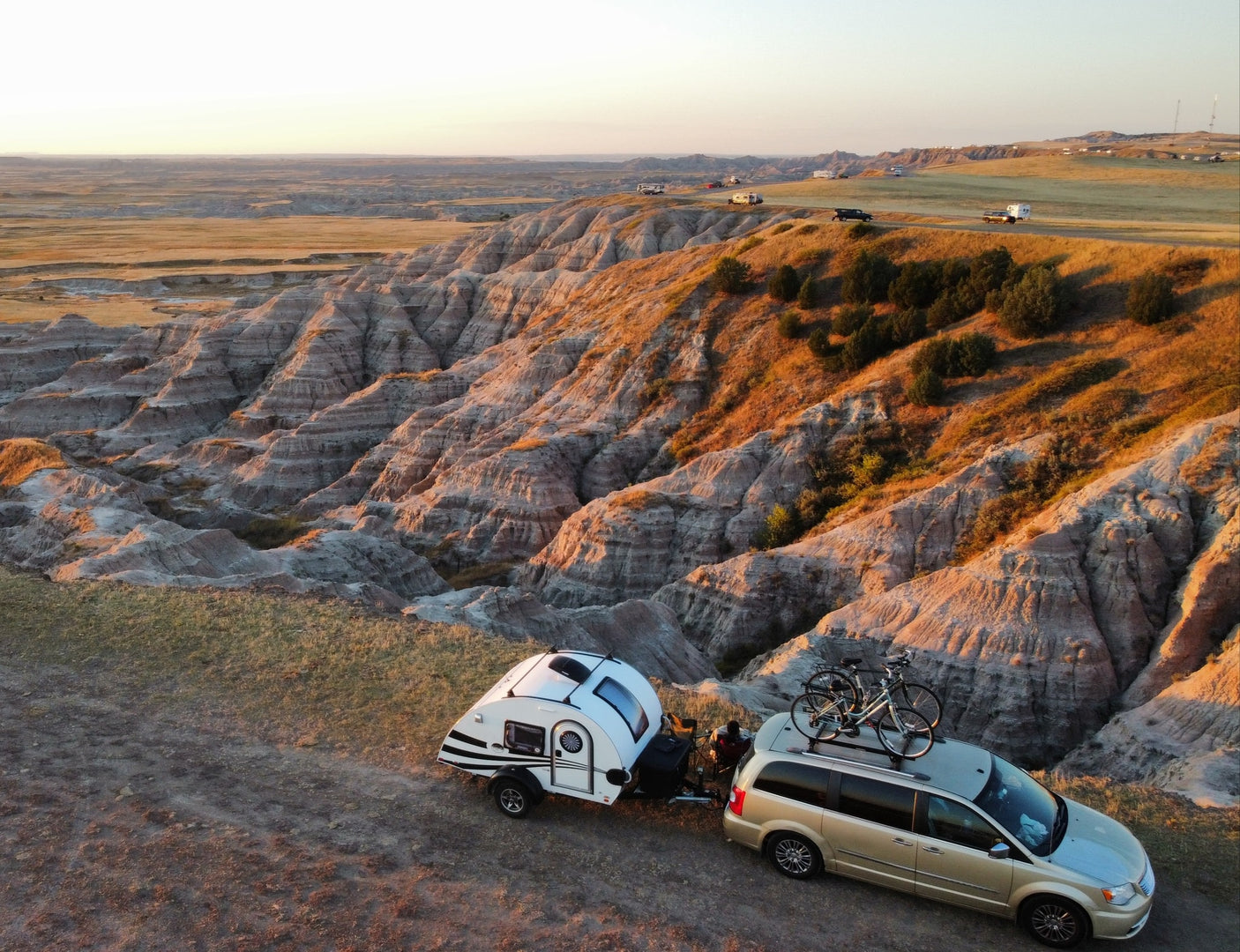 Golden minivan with rooftop bikes and teardrop RV rental setup at a breathtaking badlands overlook