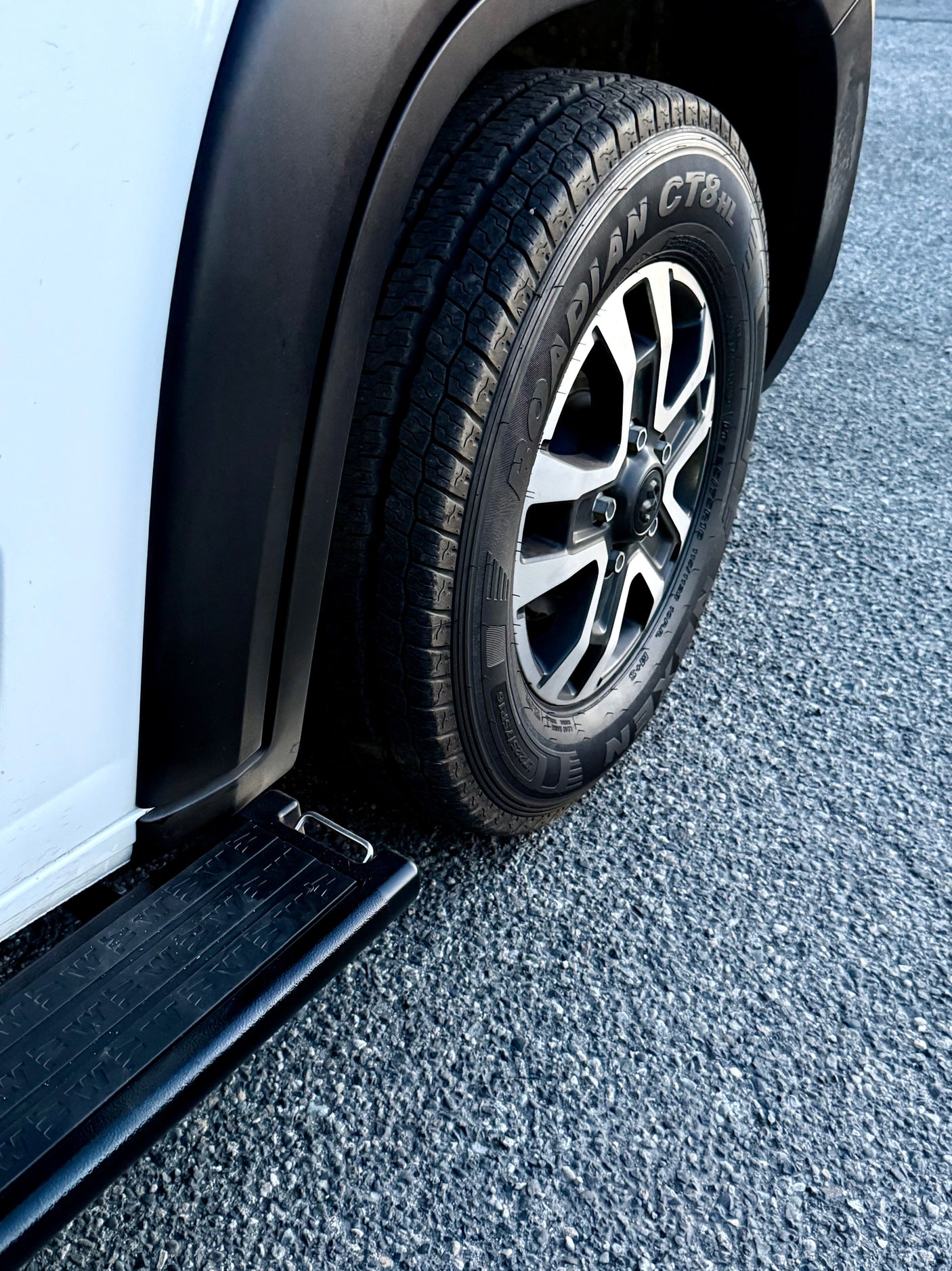 White RV rental van: tire, multi-spoke wheel, and running board on asphalt, showing vehicle detail.
