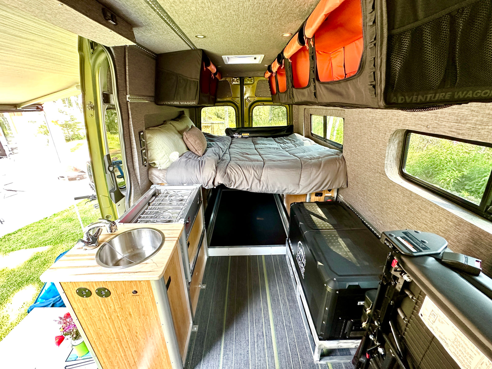RV rental van interior features a cozy bed, kitchenette with sink/stove, and overhead storage for adventurers.