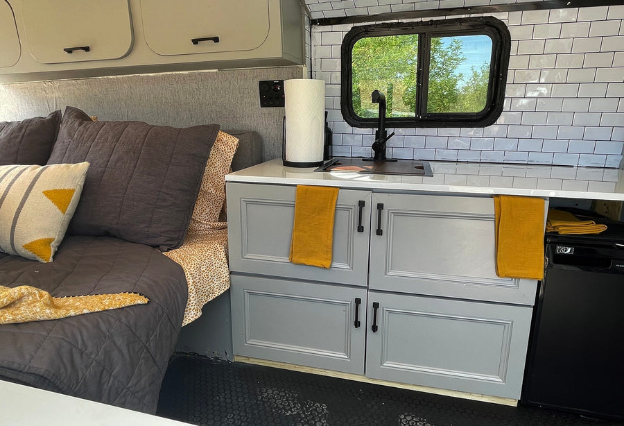 Stylish RV rental interior with a cozy bed, modern kitchenette featuring white subway tiles, and grey cabinets.