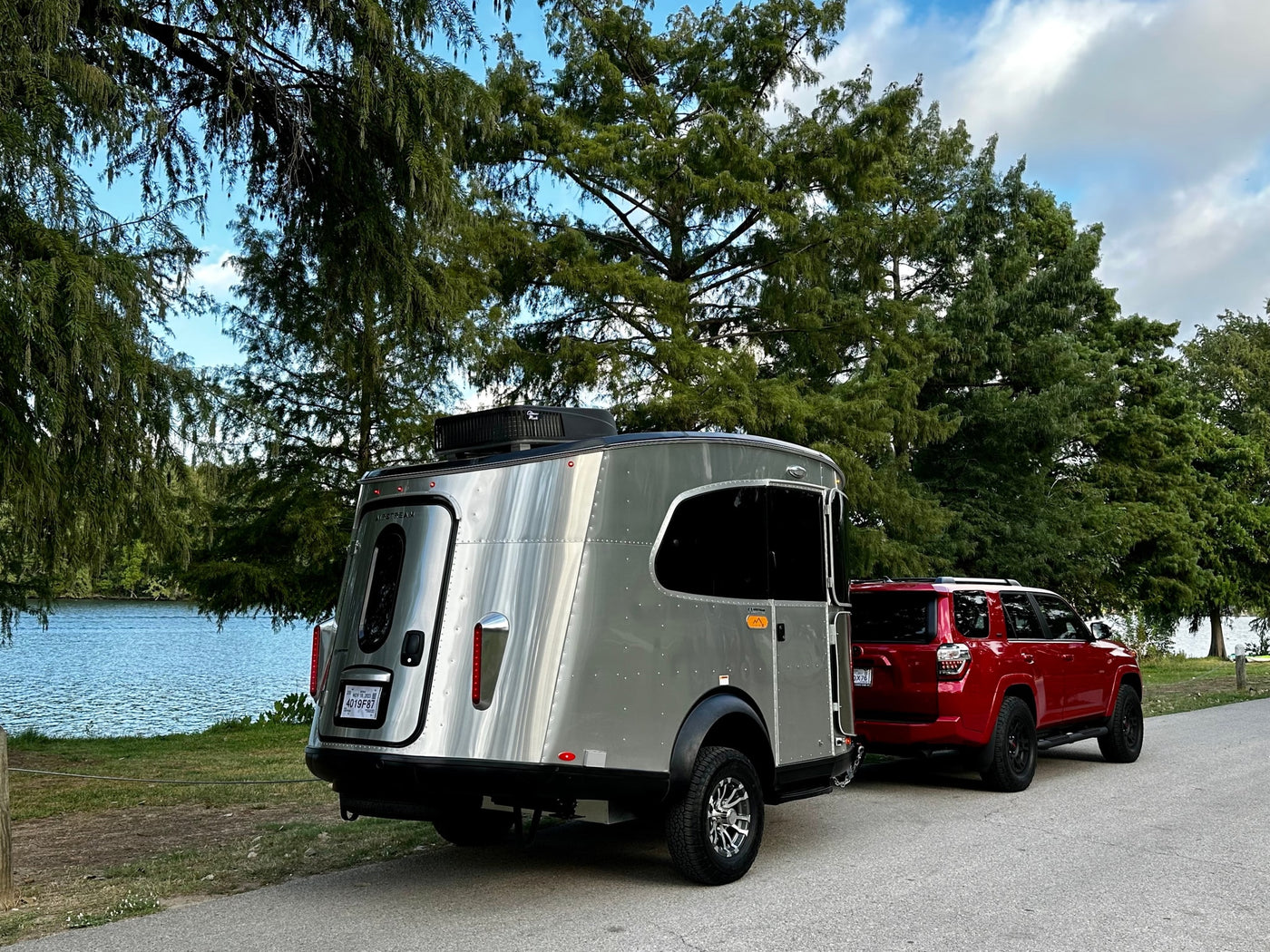Red SUV towing a sleek silver Airstream camper by the water. Explore nature with this RV rental setup!|Red SUV towing a sleek silver travel trailer — photo 1