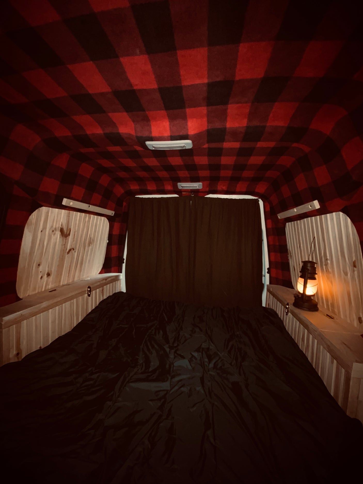 Cozy RV rental interior: red buffalo plaid ceiling, wooden paneling, a dark bed, and a lit lantern.
