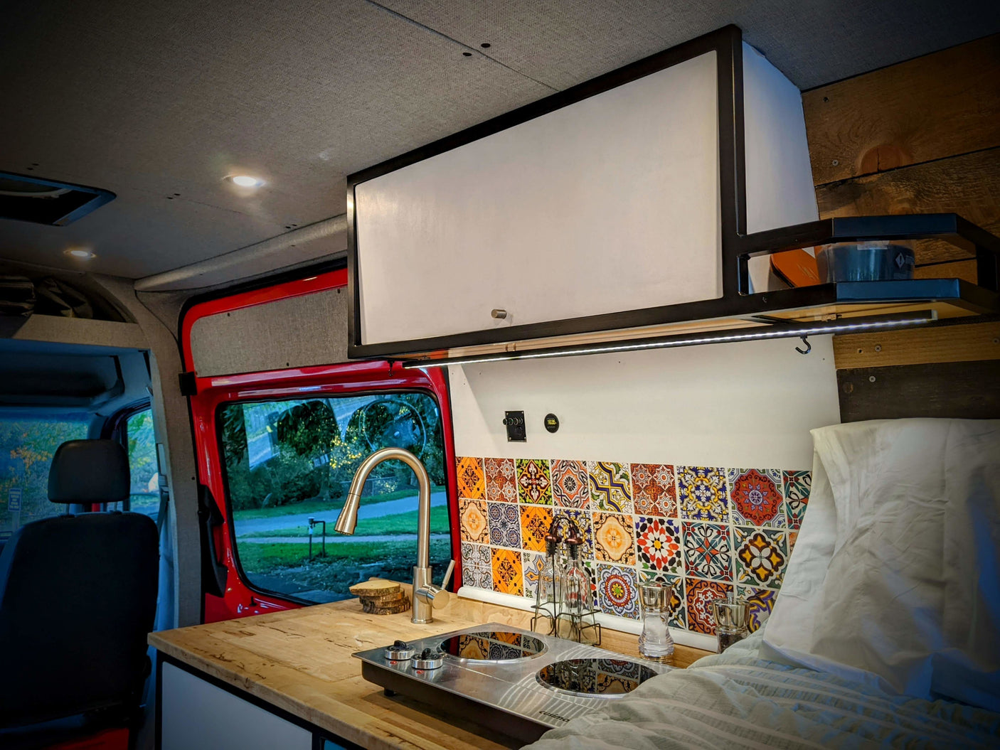 Explore this RV rental's cozy interior: a converted camper van kitchen with a colorful tiled backsplash, sink, and cooktop.