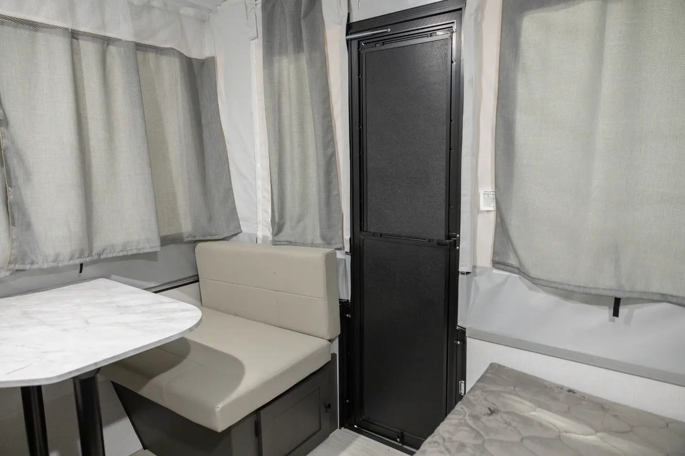 Cozy RV rental interior with a light dining booth, table, and a black entry door, surrounded by grey curtains.