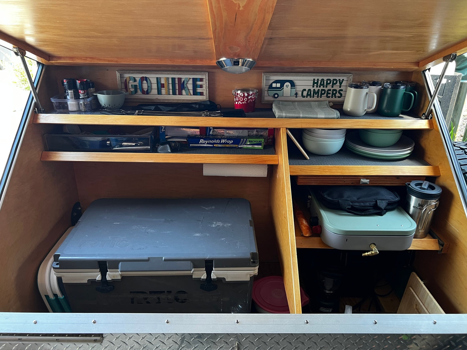 This organized rv rental kitchen galley features a cooler, camping stove, dishes, and spices, perfect for outdoor adventures.