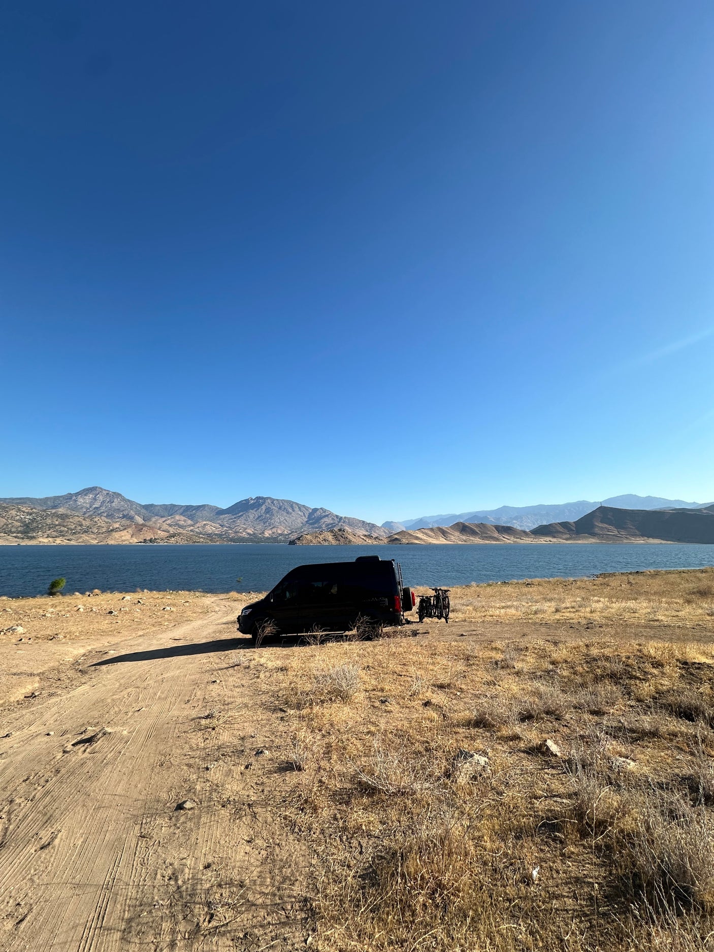 RV rental parked by a serene lake with scenic mountains and bikes, ready for an outdoor adventure.