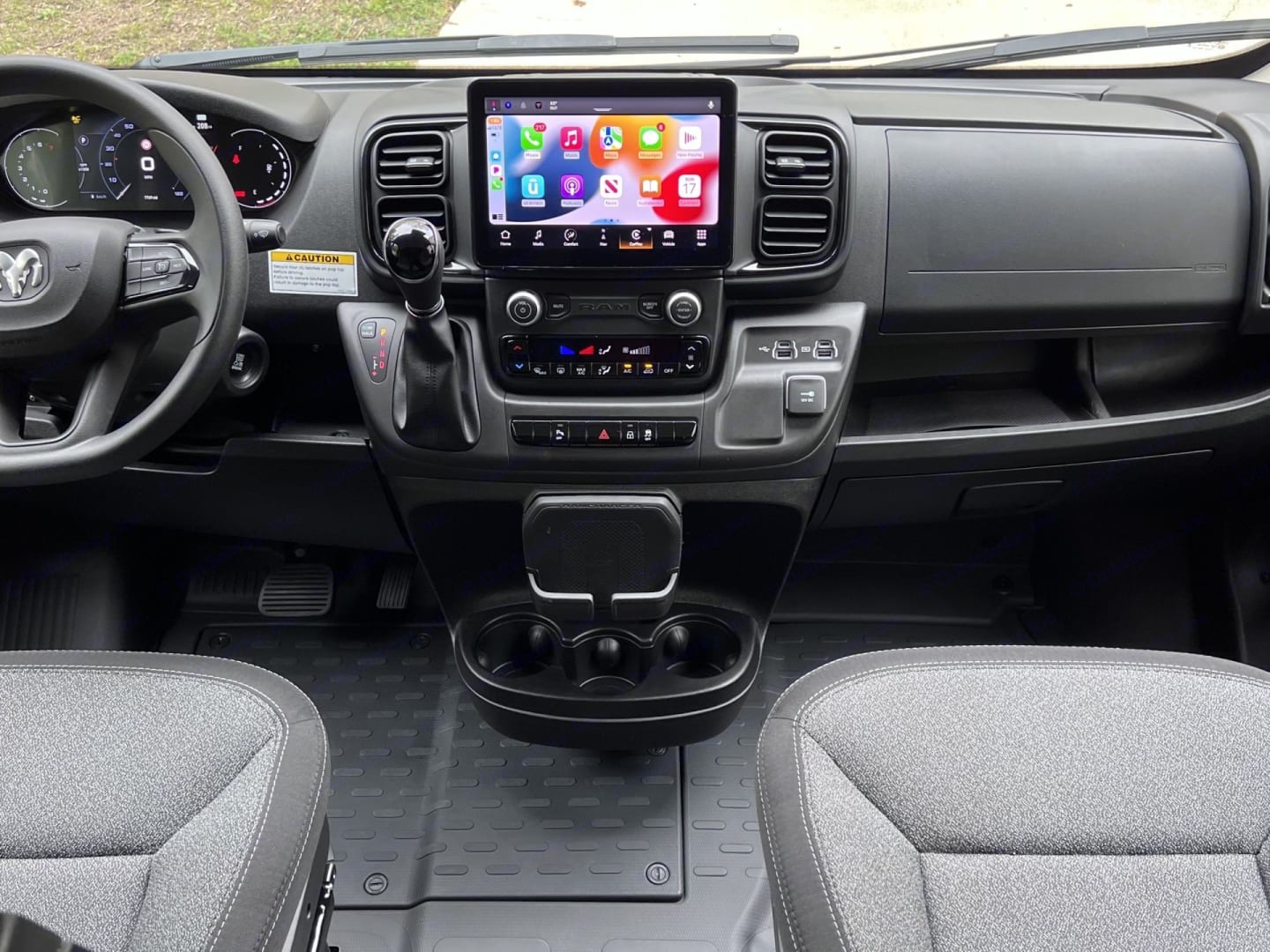 Modern RV rental interior: driver's view of the dashboard, large digital touchscreen, gear shifter, and front seats.