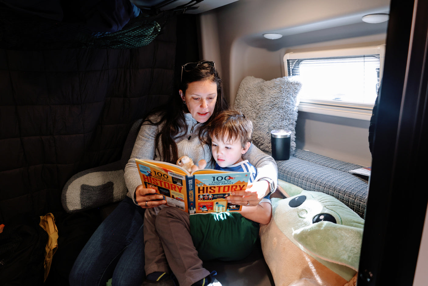 Inside an RV rental, a mother and son read a history book together.