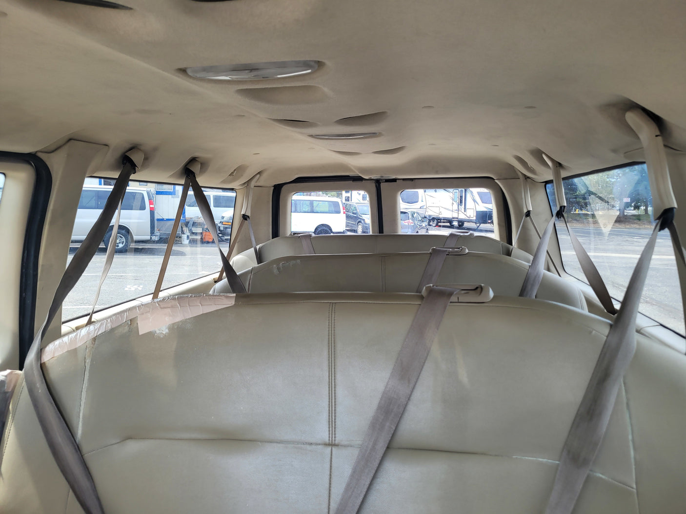 Spacious van interior with passenger seats & seatbelts, ideal for RV rental adventures. Other RVs are visible outside.