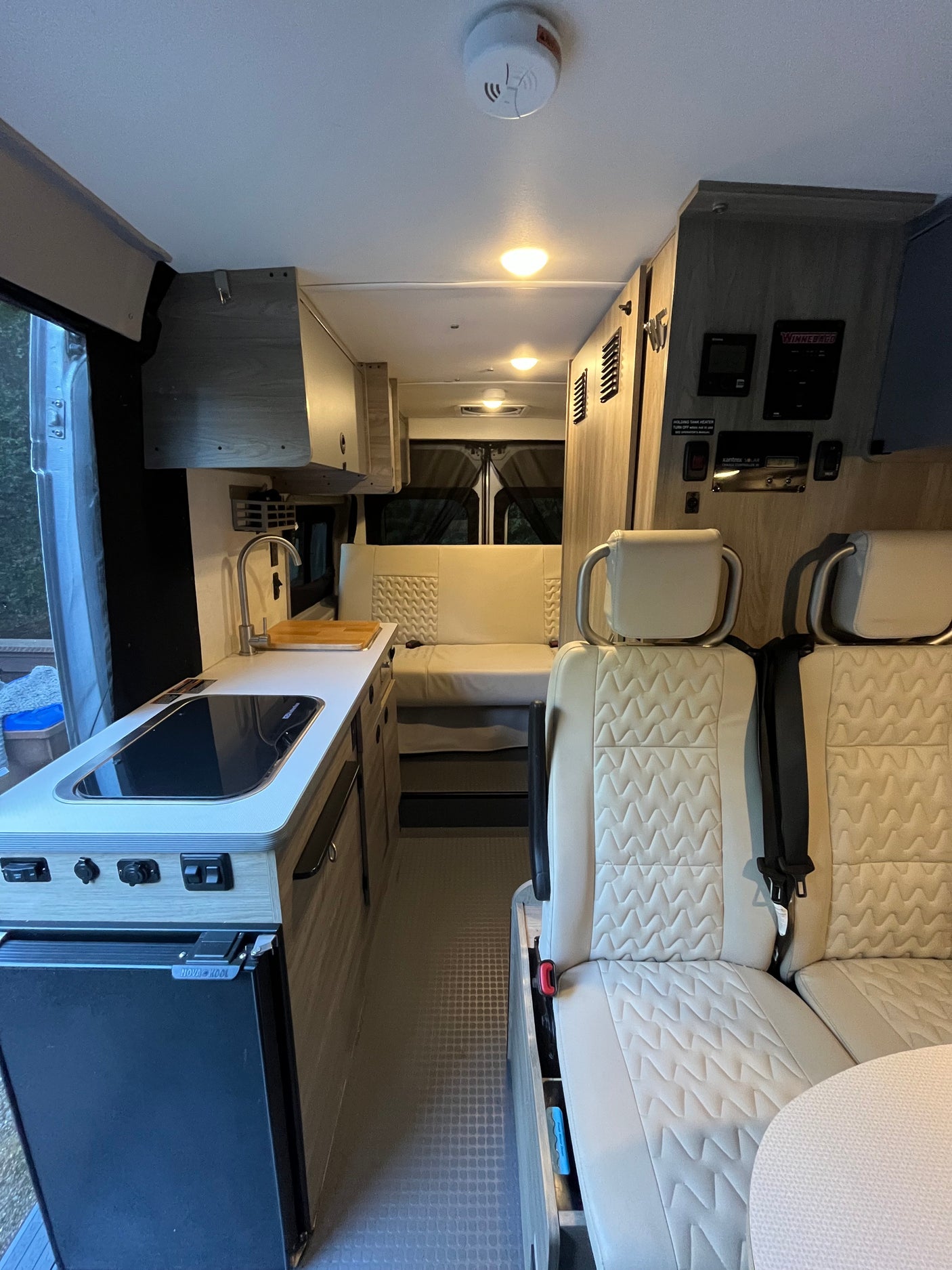 Well-lit RV rental interior with a modern kitchenette, quilted seating, and control panels.