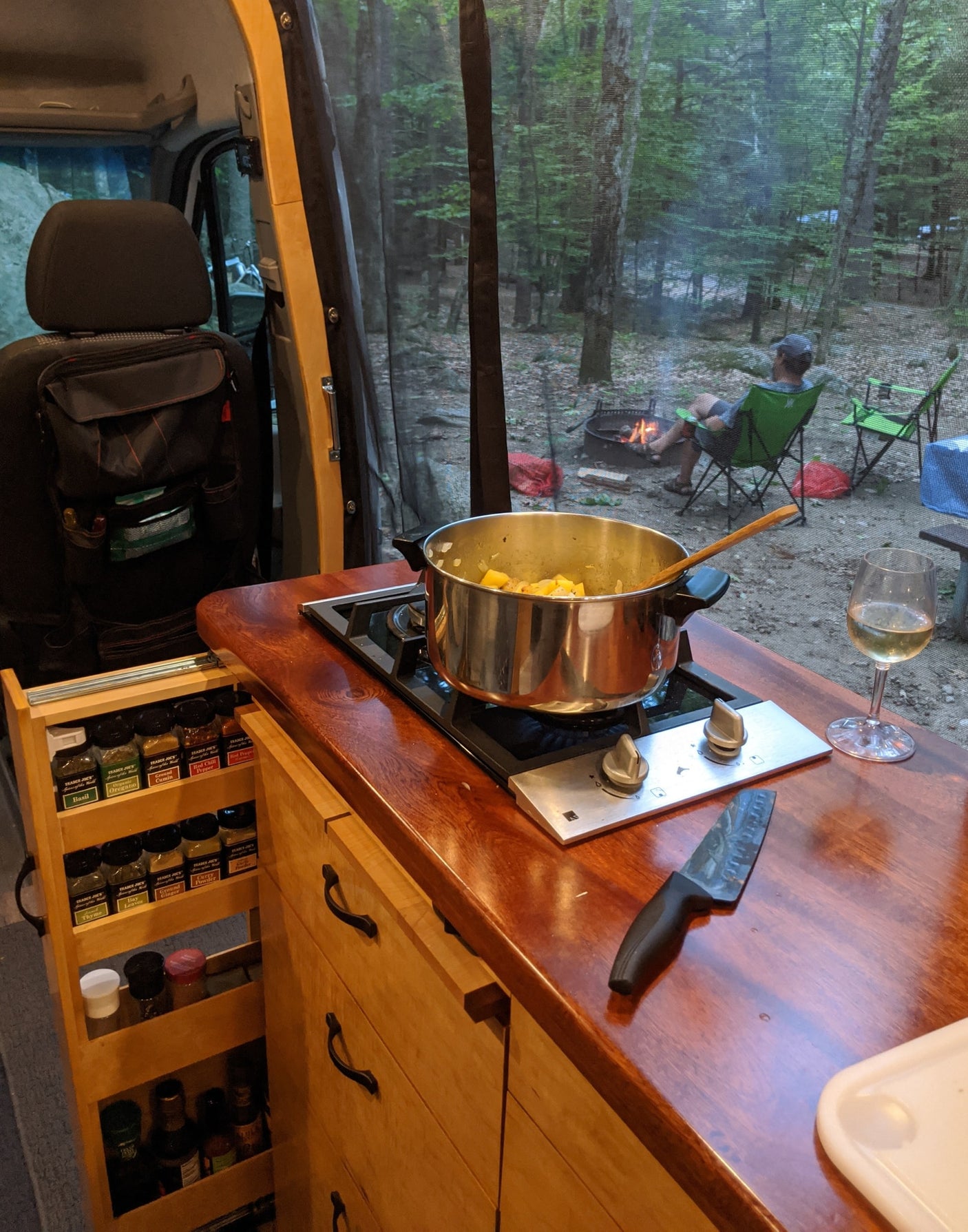 Cozy RV rental cooking: prepping dinner on the stove with a campfire view and a glass of wine.