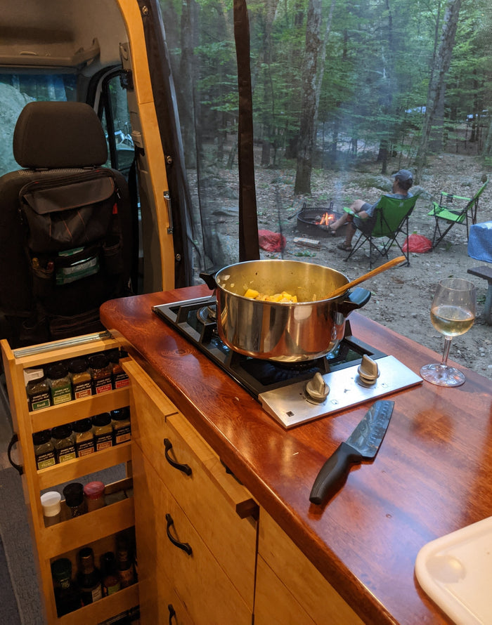 Cozy RV rental cooking: prepping dinner on the stove with a campfire view and a glass of wine.