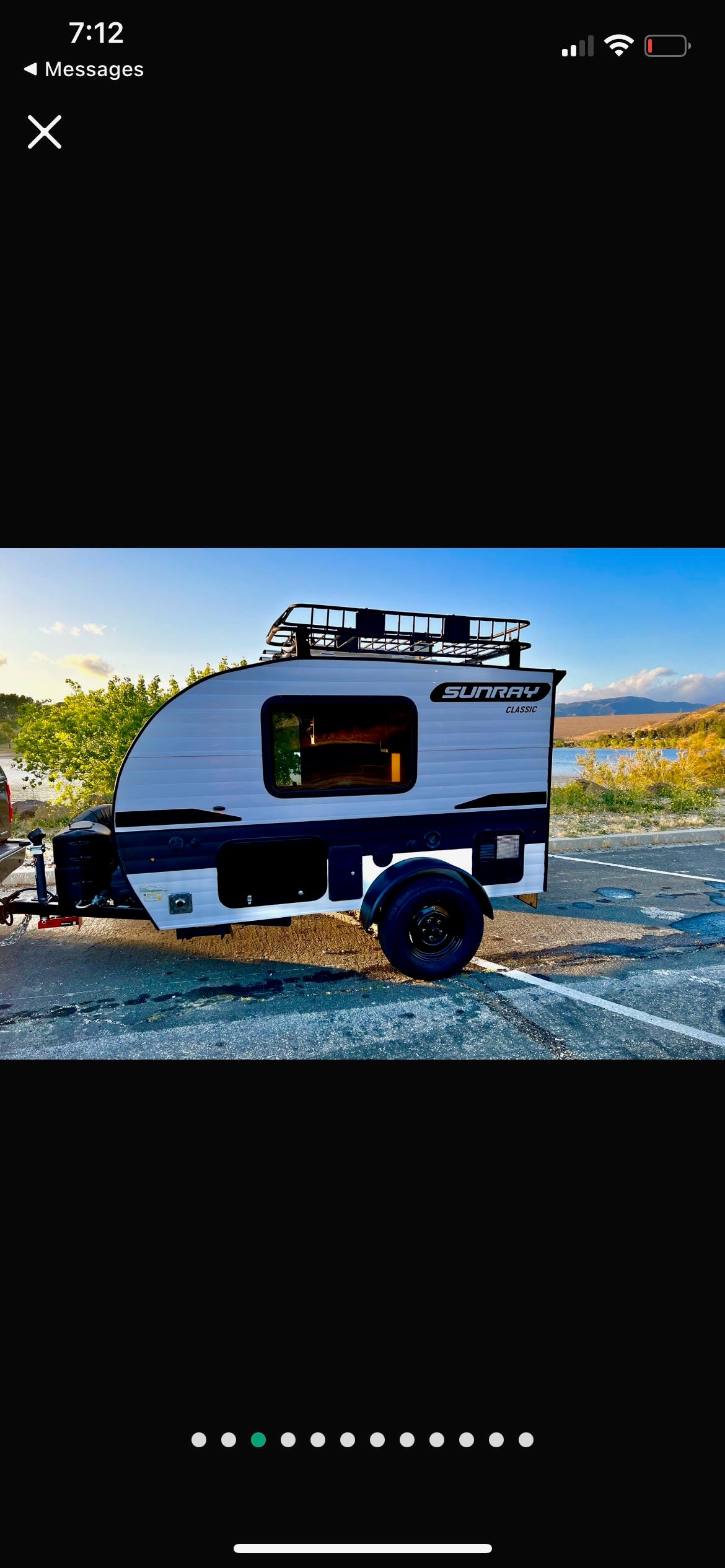 White and black Sunray Classic teardrop **rv rental** with a roof rack, parked by a scenic lake. Perfect for camping! — photo 2