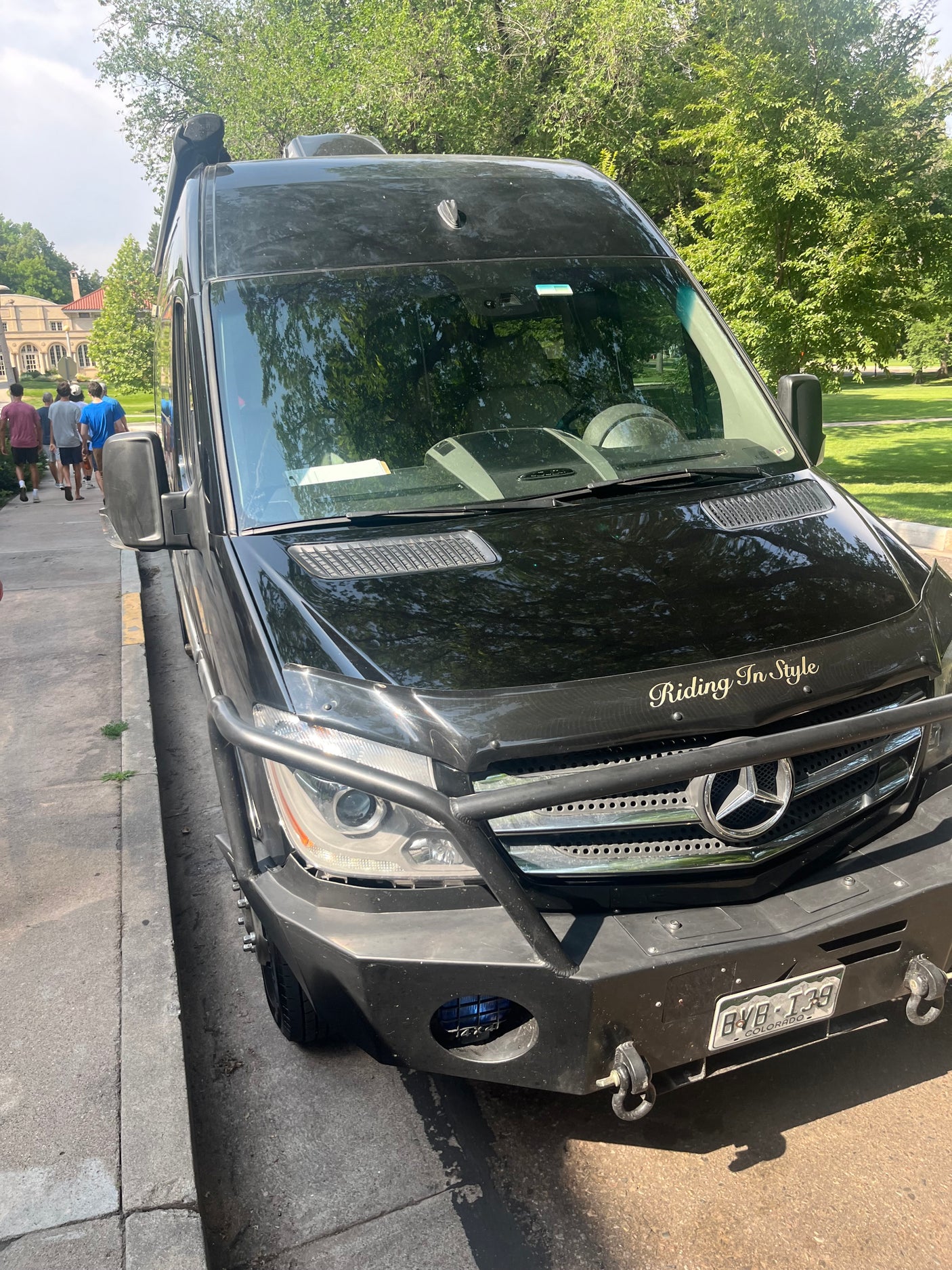Front of a custom black Mercedes Sprinter, an RV rental, with a heavy-duty bumper & "Riding In Style" text.