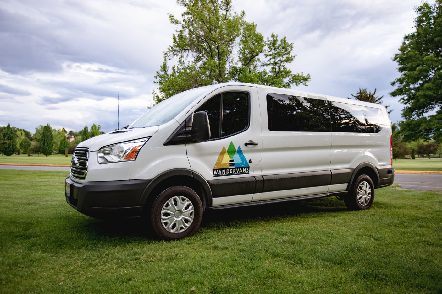 This white WANDERVANS rv rental van, with its mountain logo, is parked on green grass, ready for adventure.