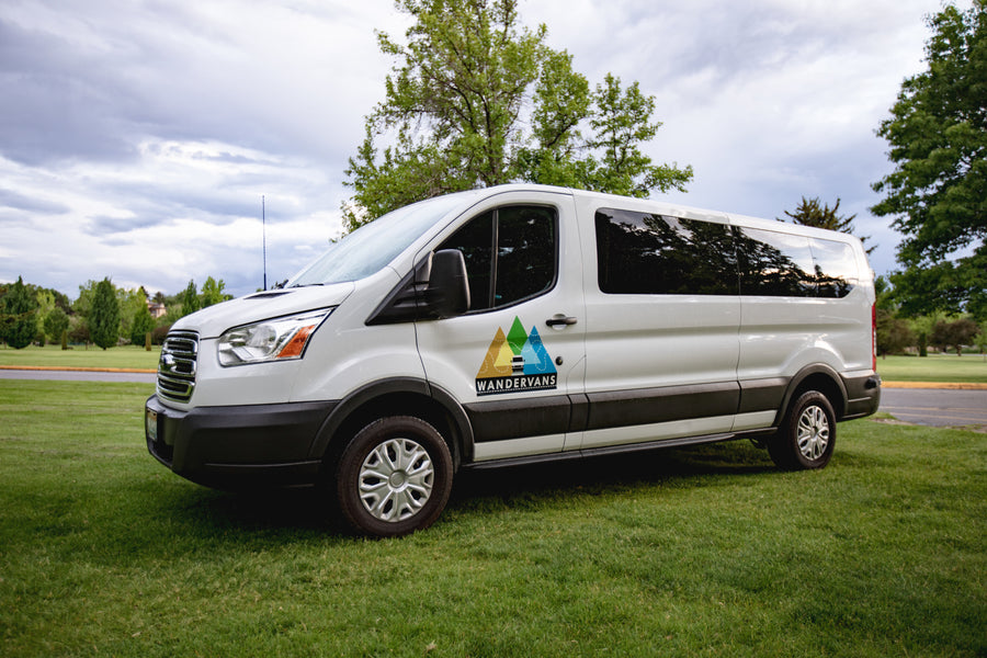 This white WANDERVANS rv rental van, with its mountain logo, is parked on green grass, ready for adventure.