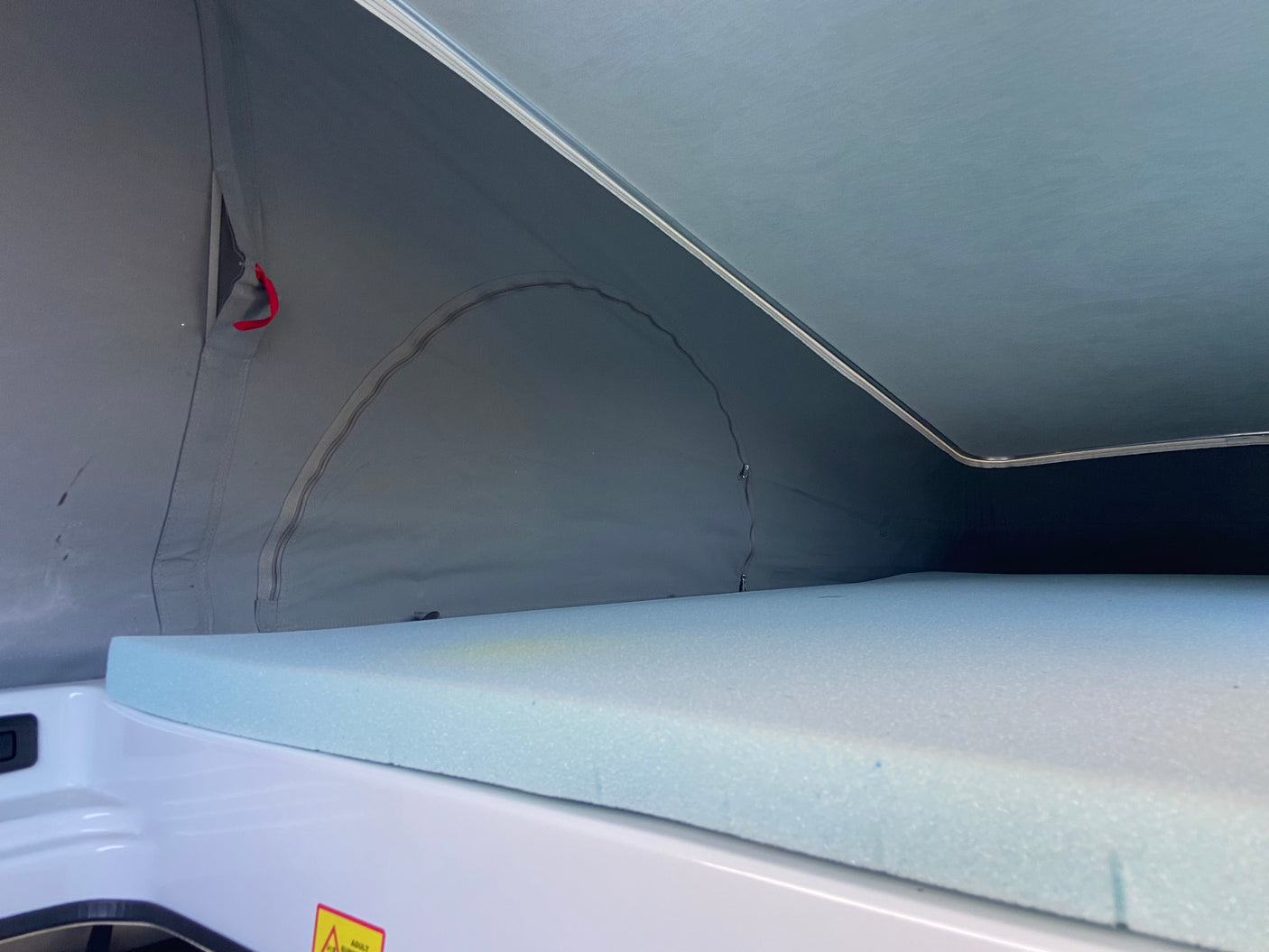Interior view of a pop-top rv rental: comfy blue foam mattress in the sleeping area, surrounded by grey canvas.