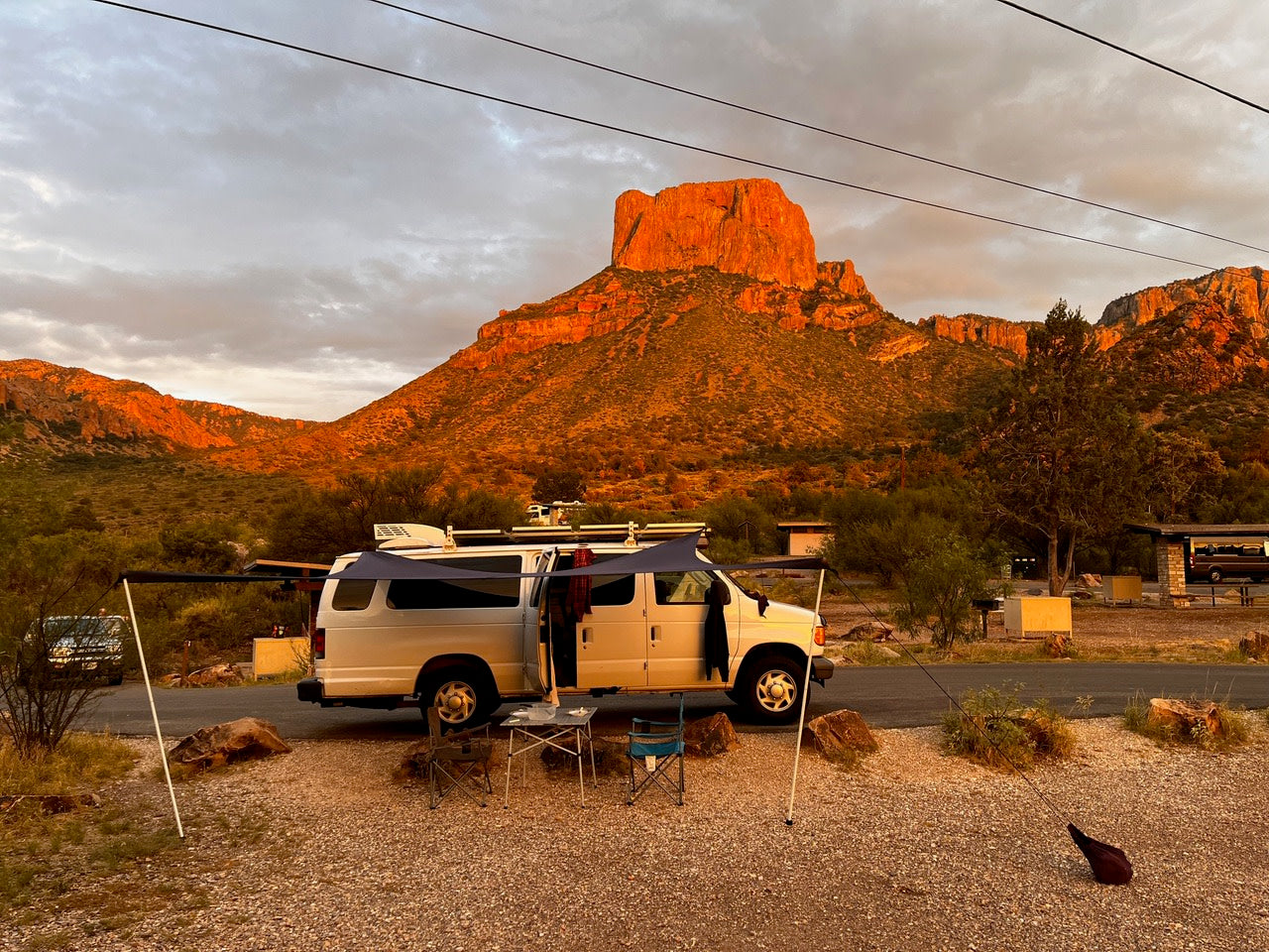 Stunning RV rental camping adventure! White campervan with awning at a scenic desert mountain campsite at sunset.