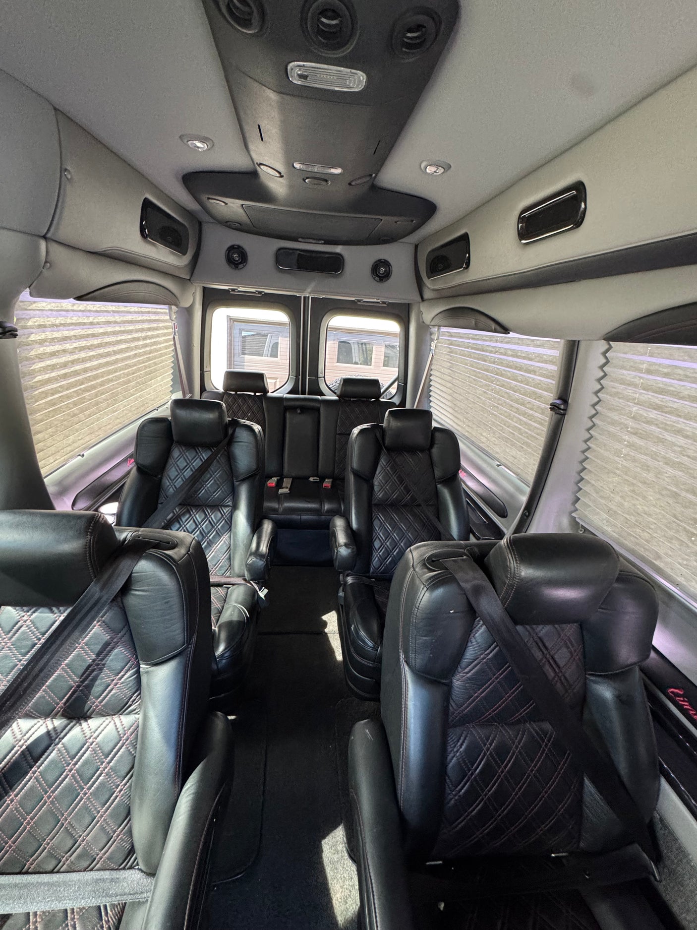 Inside a premium RV rental: comfortable black quilted leather captain's chairs & rear bench with window blinds.