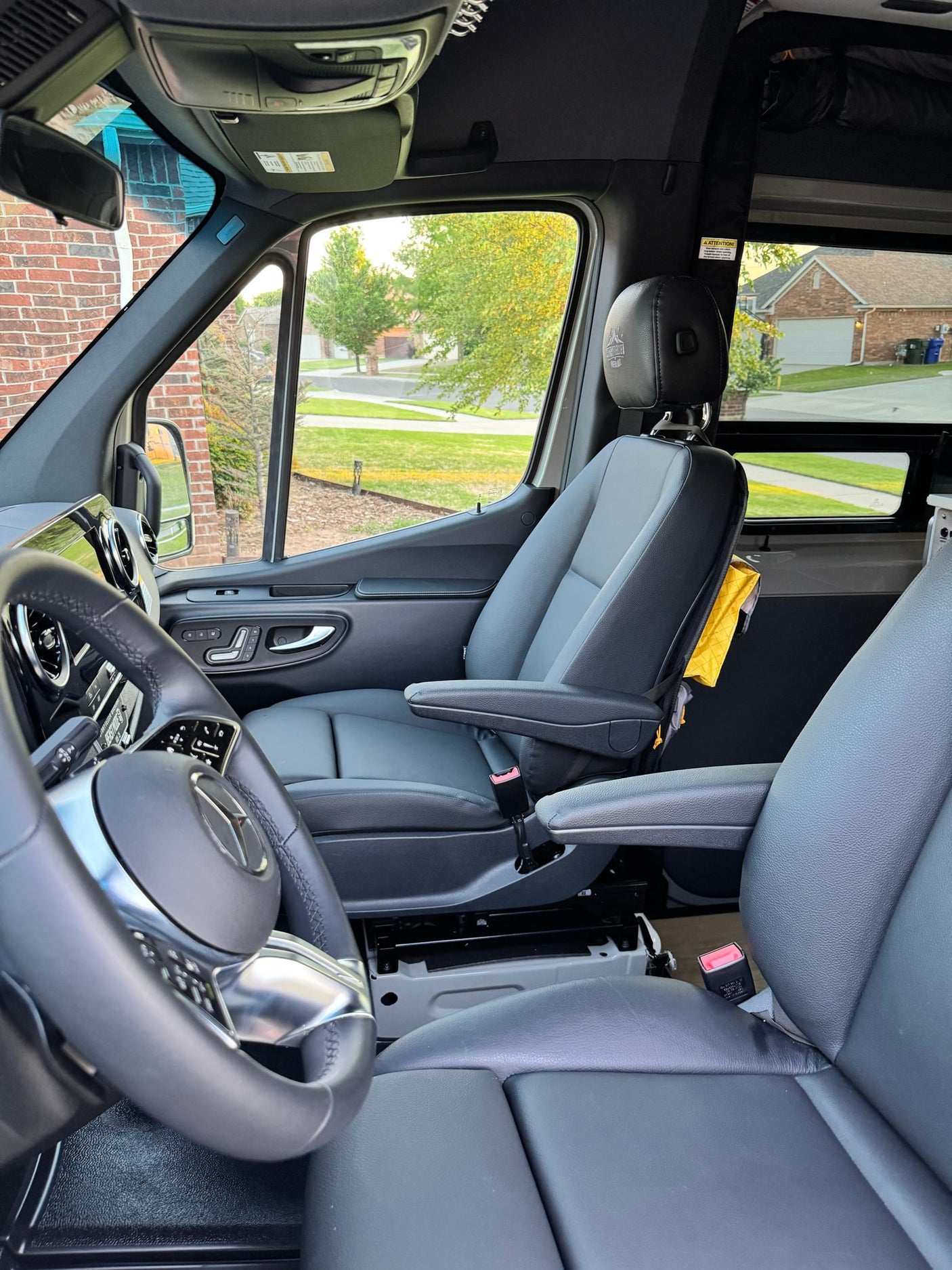Driver's view of a modern rv rental camper van cabin, showcasing the steering wheel, passenger seat, and outside residential street.