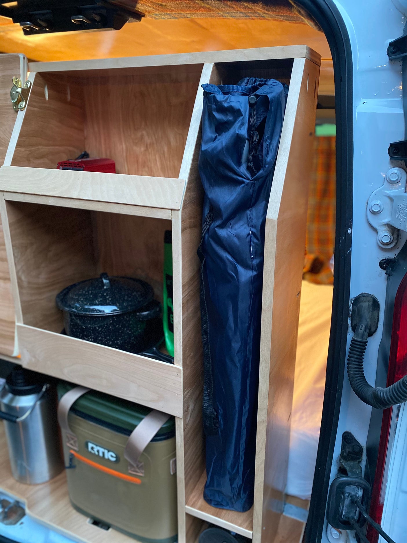 Organized camper van interior with custom wooden storage, an RTIC cooler, and cooking gear. Great for rv rental adventures!
