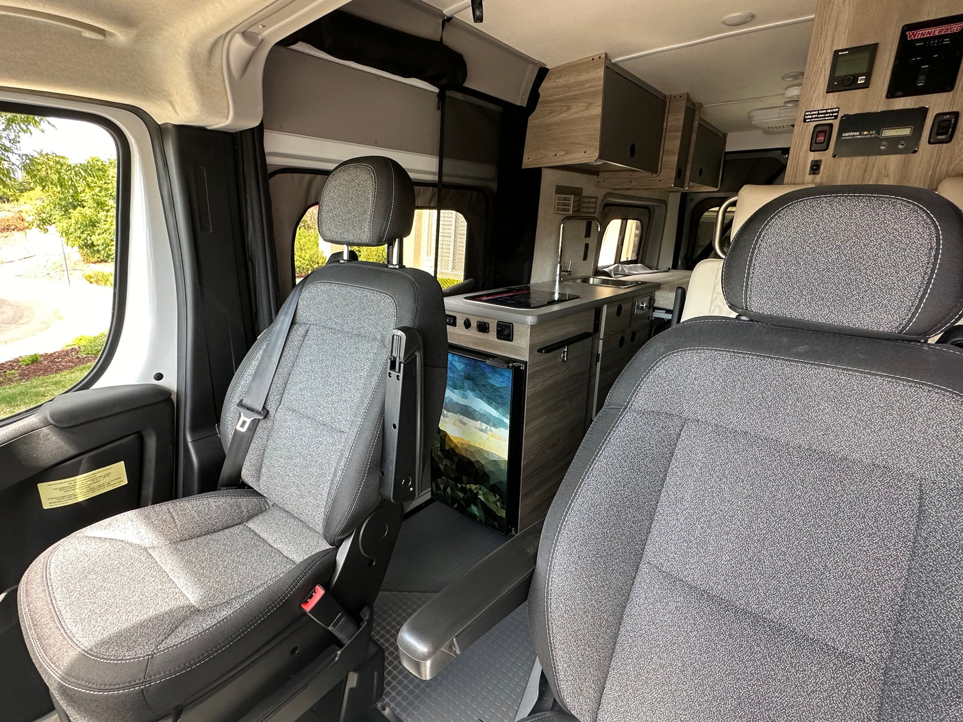 An rv rental interior showing front passenger seats, a well-equipped kitchenette with sink and fridge, plus overhead controls.