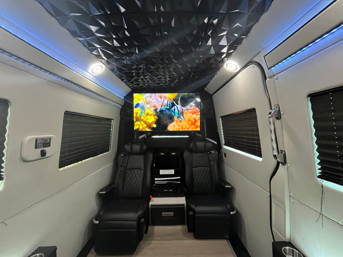 Inside a premium RV rental: plush black captain's chairs, large TV with fish, geometric ceiling, and blue LED ambient lighting.
