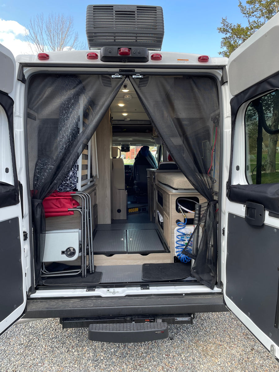 is parked with its pop-top open amidst trees.|An RV rental camper van's open side door