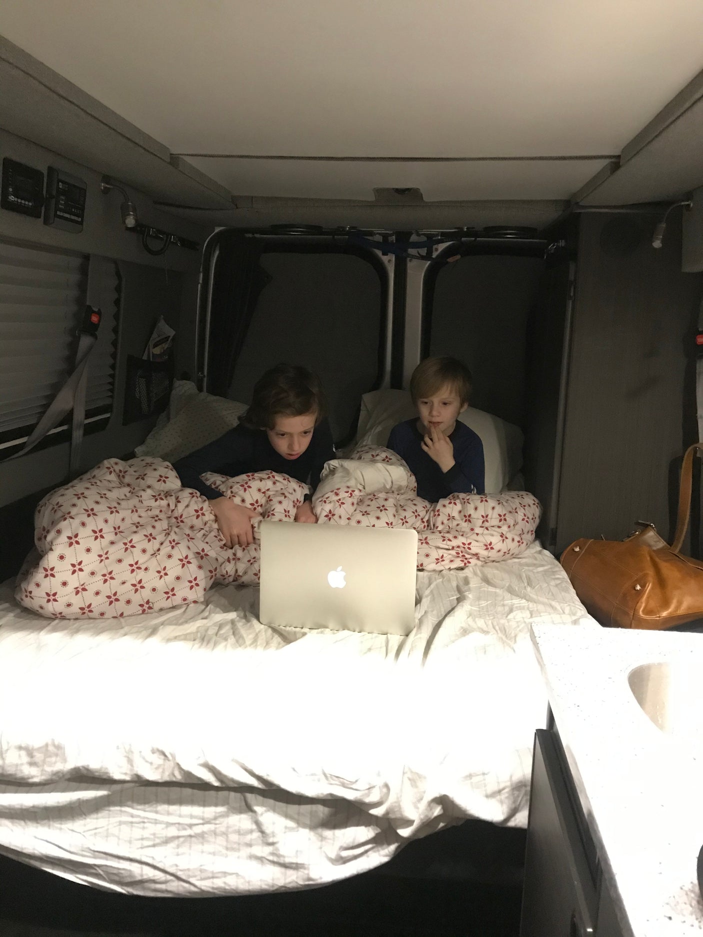 Inside an RV rental, two boys watch a laptop in their bed. A cozy setup for family travel.