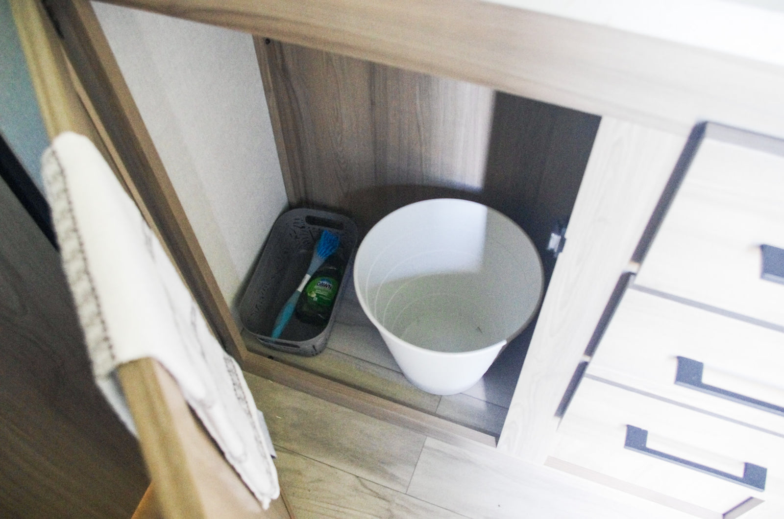 Efficient under-sink storage in this RV rental! Features cleaning supplies in a basket & a small trash bin.