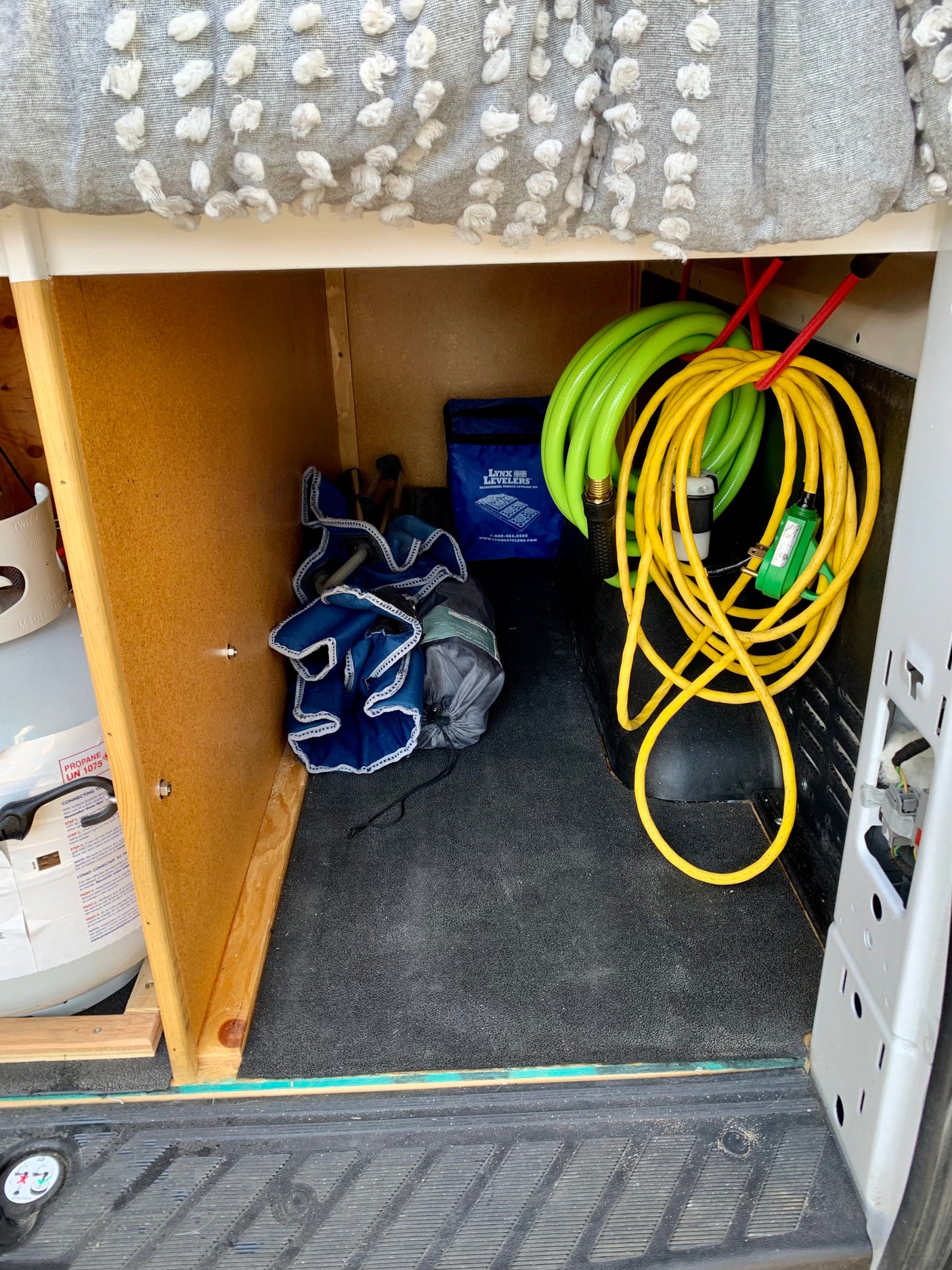 RV rental interior storage: hoses, cords, Lynx Levelers, chairs, & propane tank neatly tucked under the bed.