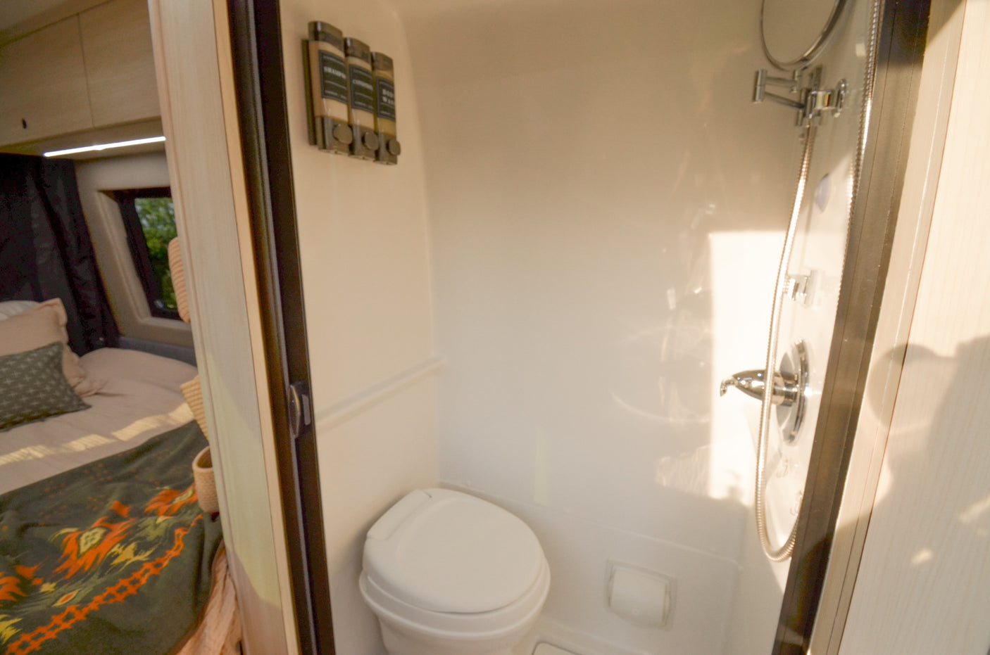 Inside an RV rental: a compact bathroom with toilet & shower, offering a glimpse into the connected cozy bedroom.