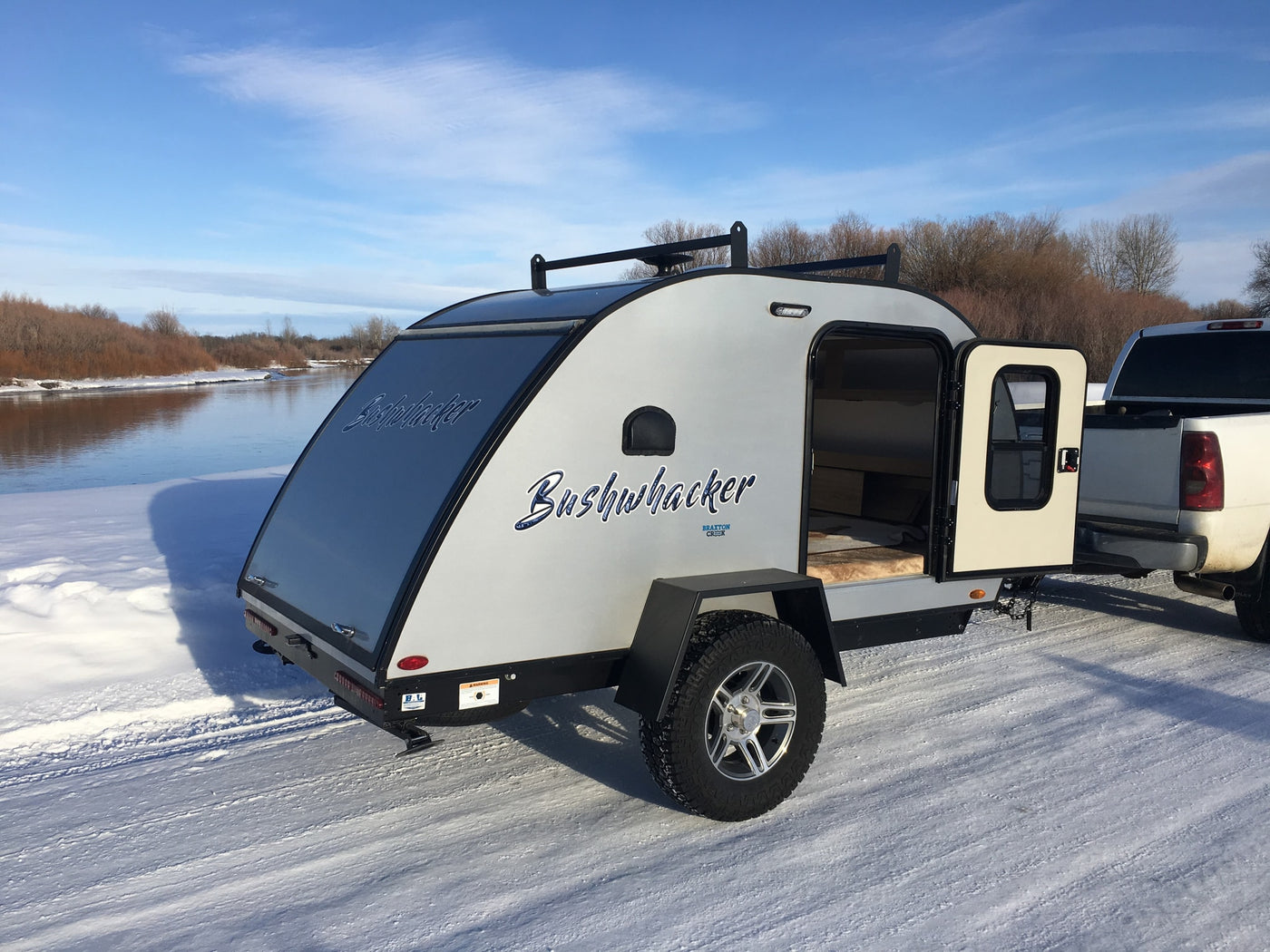 A modern Bushwhacker teardrop RV rental is parked on snowy ground by a river, ready for cold-weather camping. — photo 5