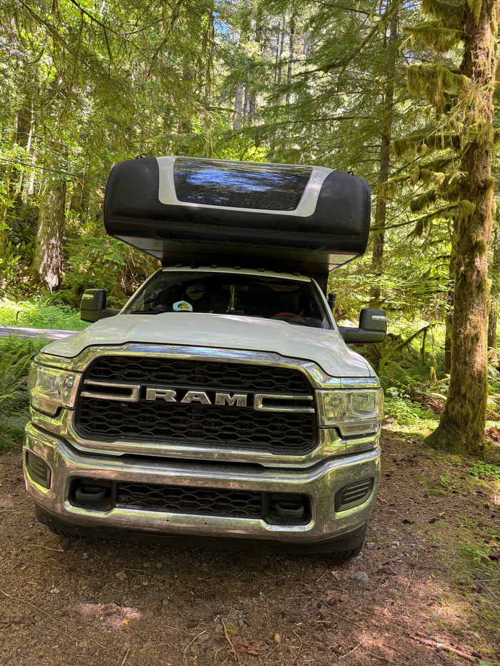 A white Ram truck with an attached camper, an ideal RV rental for a forest adventure amidst mossy trees.