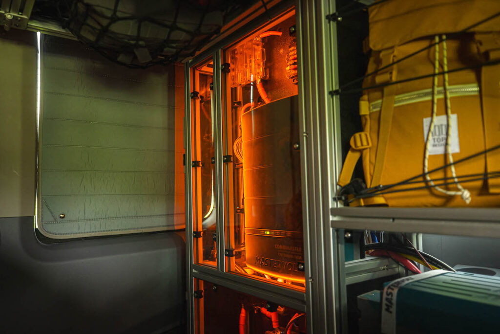 An RV rental's interior: orange-lit Mastervolt power system, insulated window, and backpack storage. Essential for off-grid adventures.