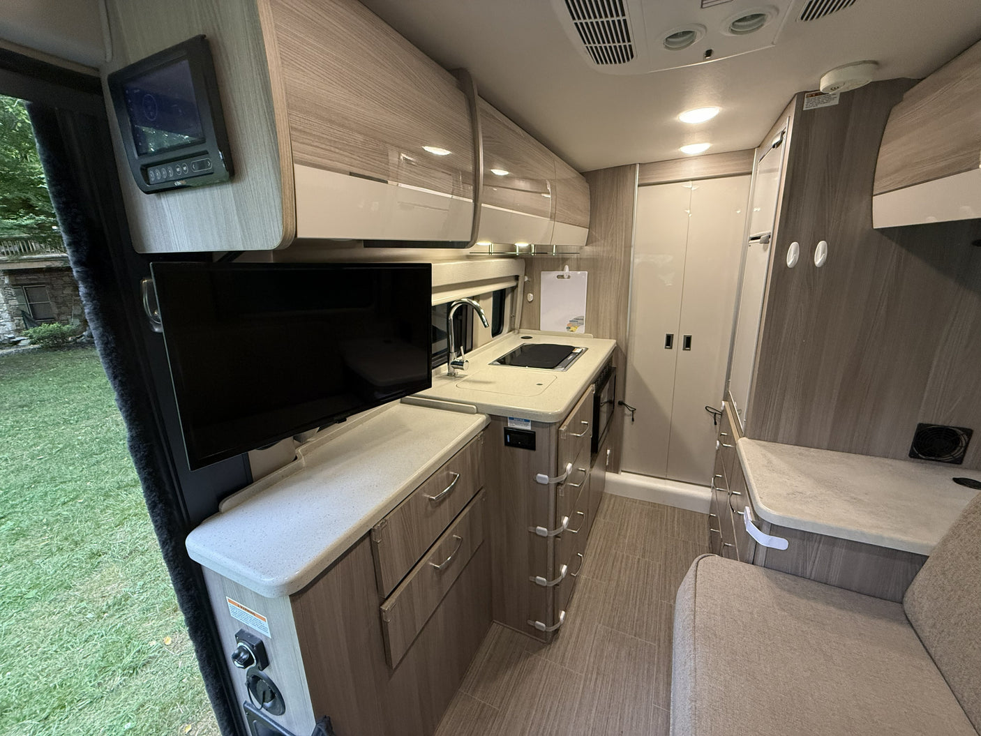 Modern RV rental interior with a kitchenette, sink, stove, TV, and light wood cabinets, plus a cozy seating area.
