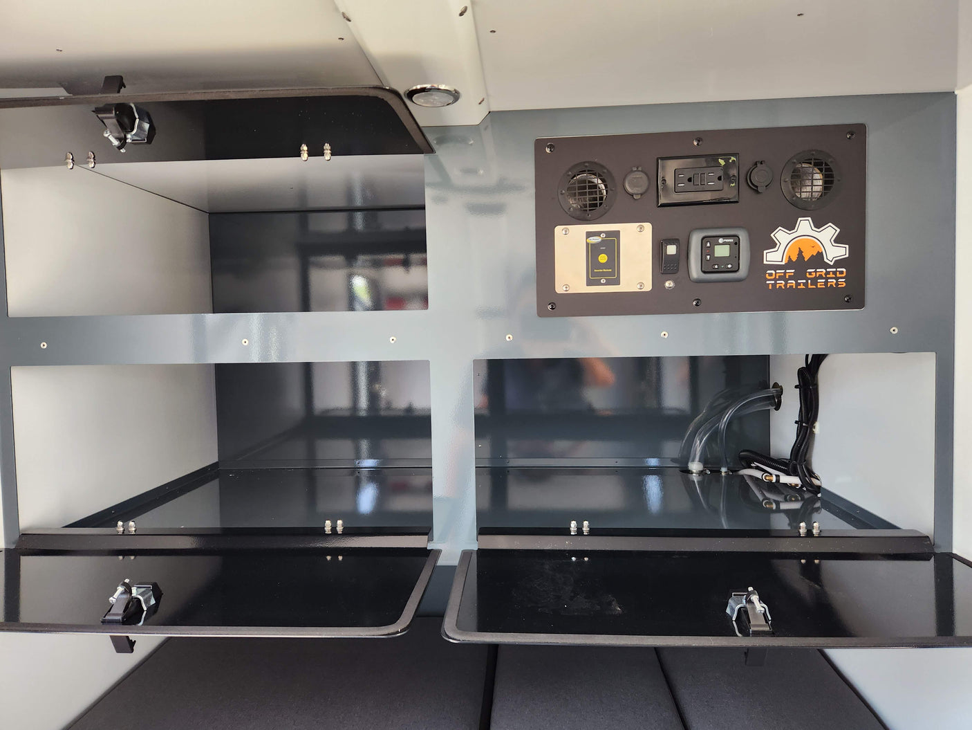 Inside an RV rental: control panel with inverter remote & heater, plus storage compartments and utility hookups. Off Grid Trailers.