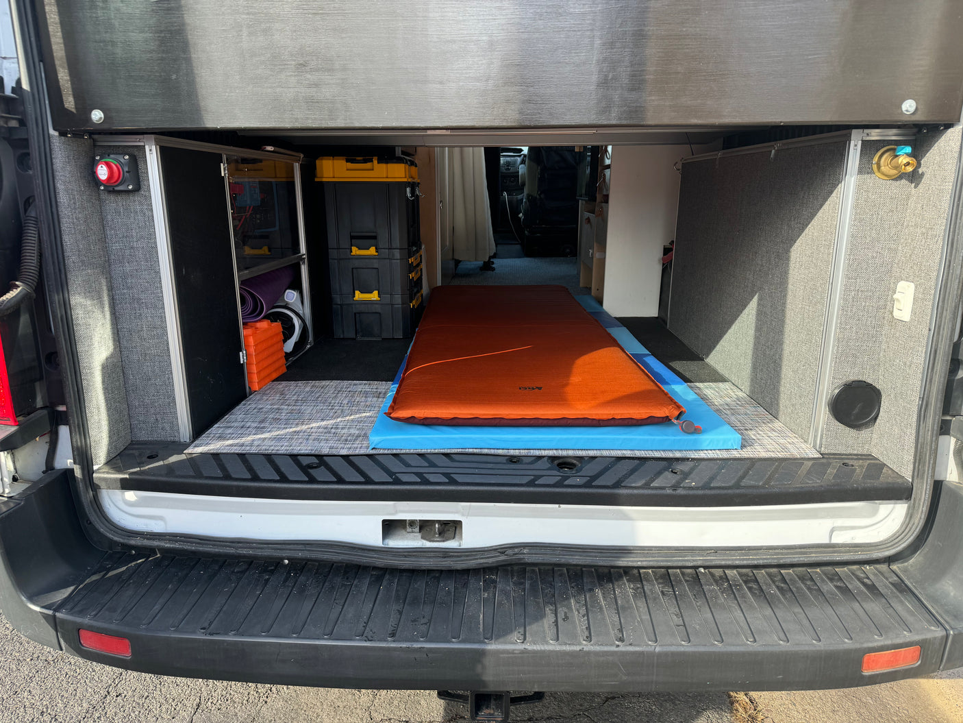 Rear interior of a custom RV rental camper van, showing a comfy bed, organized storage, and essential utilities.