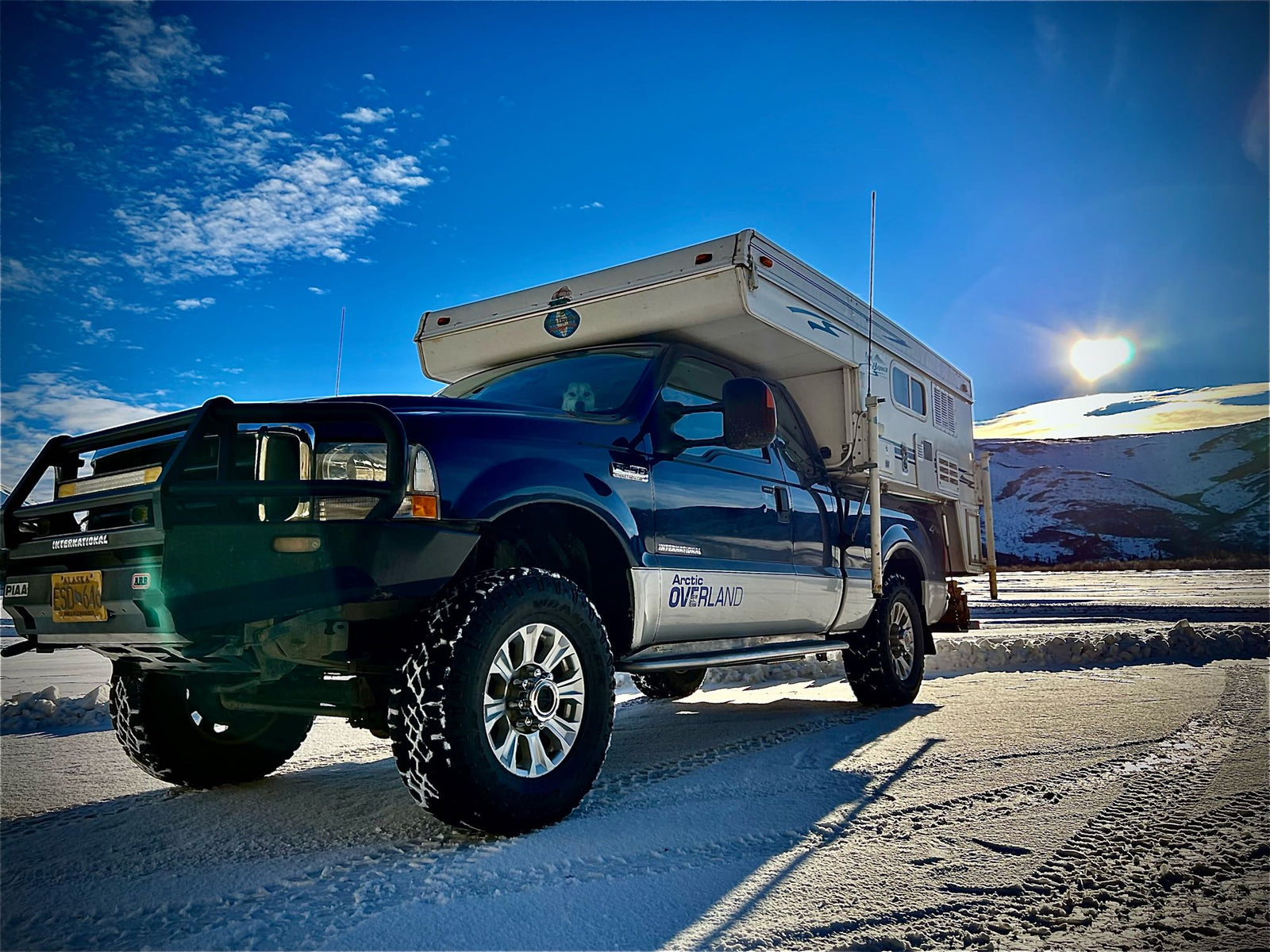 Blue Ford truck with Arctic Overland camper on snow. Heart-shaped sun. Perfect RV rental for Alaska winter trips with your dog.|Blue truck with Bronco pop-up truck camper