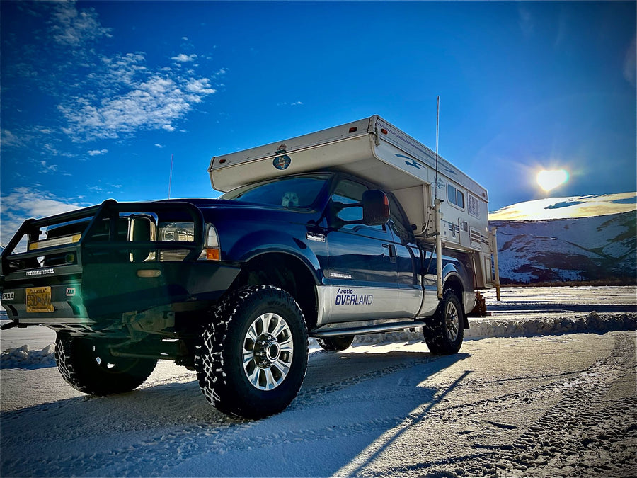 Blue Ford truck with Arctic Overland camper on snow. Heart-shaped sun. Perfect RV rental for Alaska winter trips with your dog.|Blue truck with Bronco pop-up truck camper
