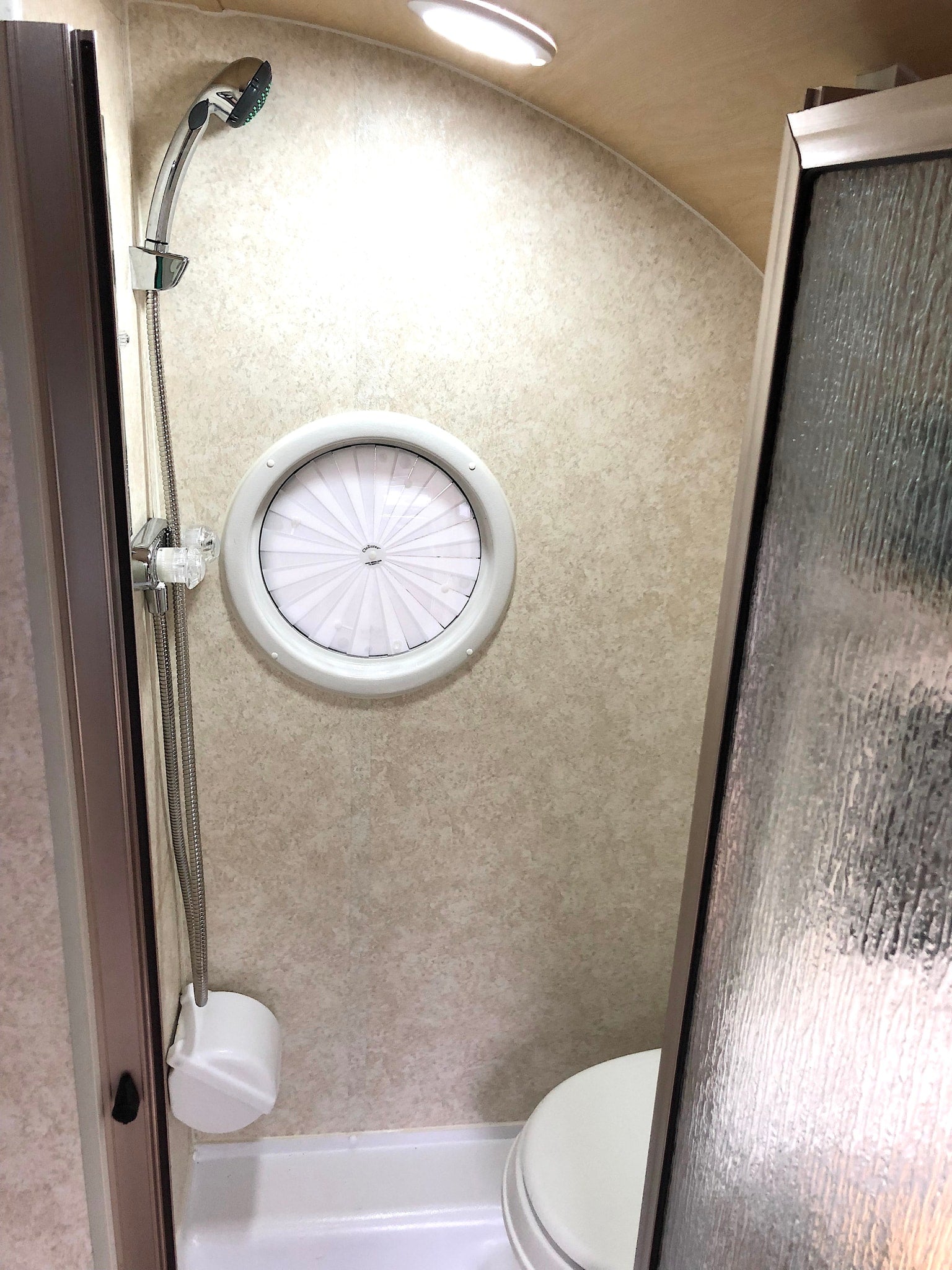 RV rental bathroom: Efficient space with a shower, toilet, and distinctive circular window, optimized for compact living.