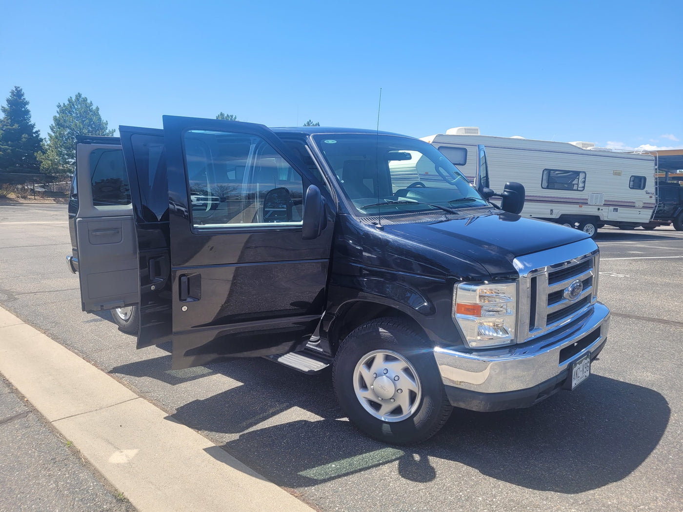 parked on asphalt near RV rental storage on a sunny day.|Black van with open doors in an RV lot. A spacious option for your next RV rental adventure or group travel.|A sleek black Ford van with doors open — photo 9