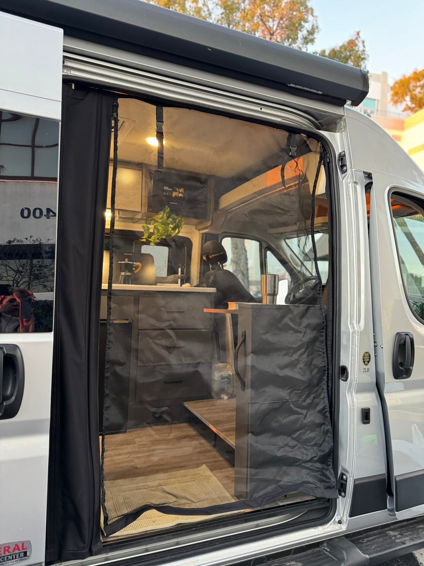 See inside an rv rental camper van: open side door, bug screen, cozy kitchen, and living area with bed.