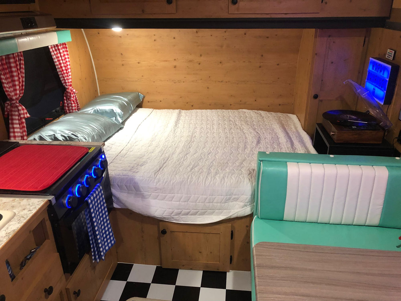 An inviting rv rental interior, showcasing a comfy bed, functional kitchen, and retro diner-style booth with a checkered floor. — photo 8