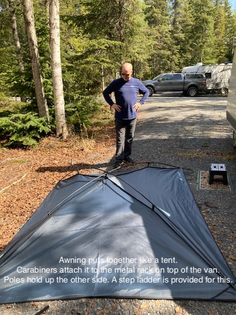 RV rental setup: Man assembling a gray, tent-like awning at a wooded campsite. It attaches to the vehicle's roof rack. — photo 17