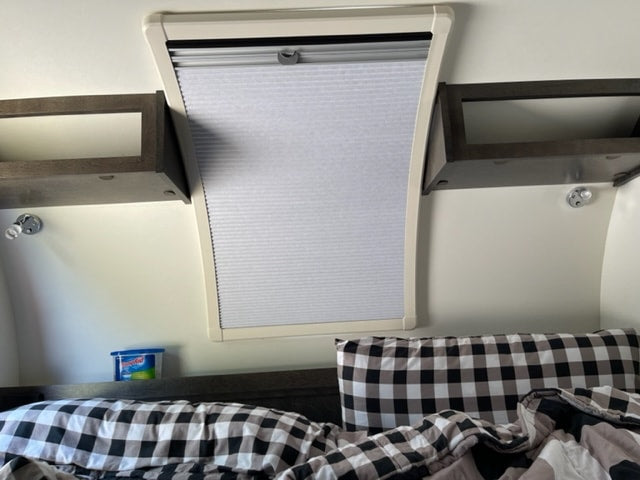Cozy RV rental bedroom with checkered bedding, a window with a shade, and bedside storage shelves and lights.