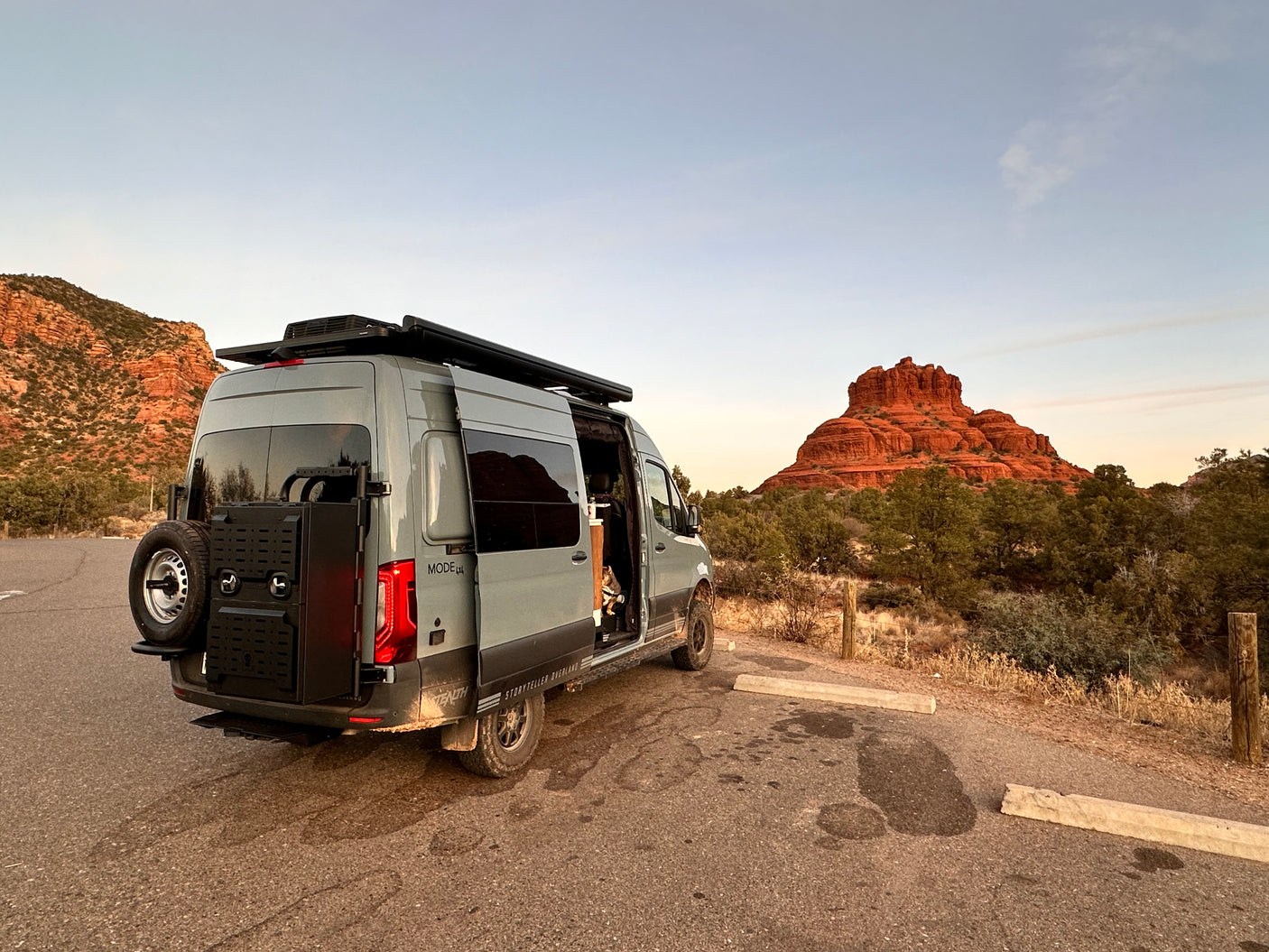 Adventure awaits! This grey RV rental camper van is parked amidst Sedona's stunning red rocks with a dog on board.