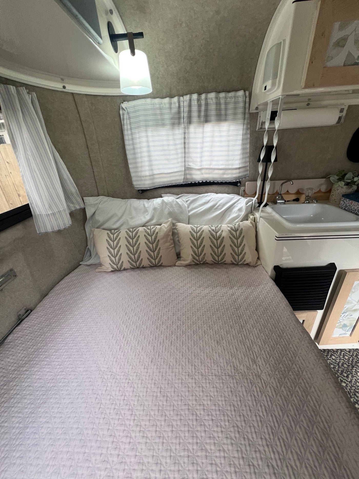 Bright RV rental interior showing a comfortable bed with neutral bedding, patterned pillows, and a small sink. — photo 8