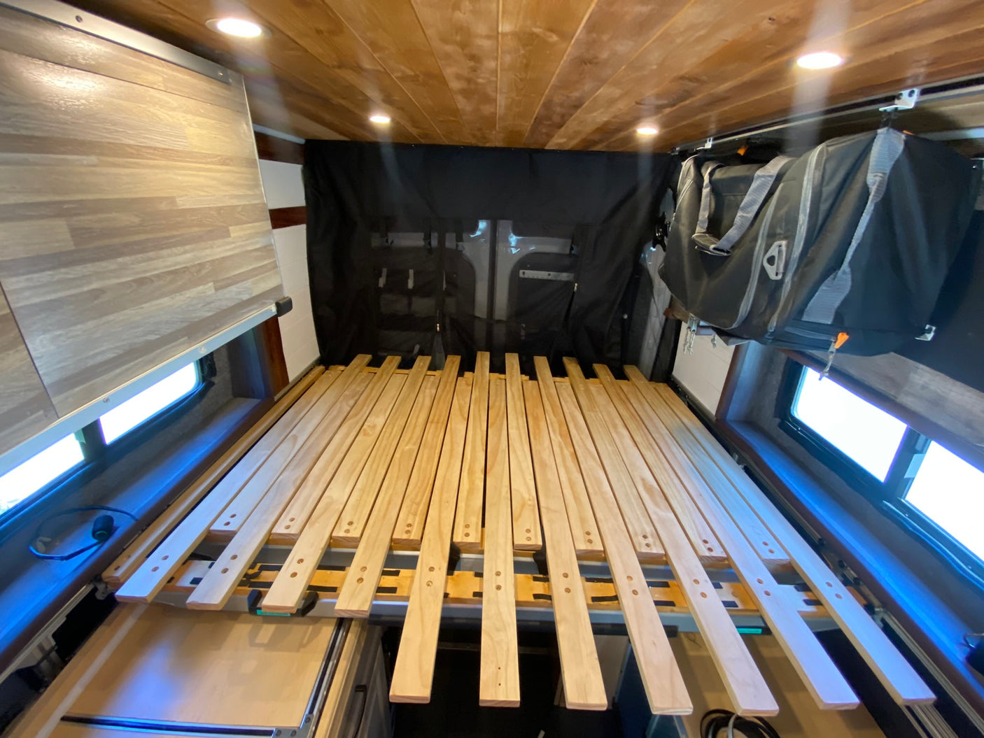 RV rental: Slatted bed base, hanging storage, and wood-paneled interior. Ideal for van life adventures.